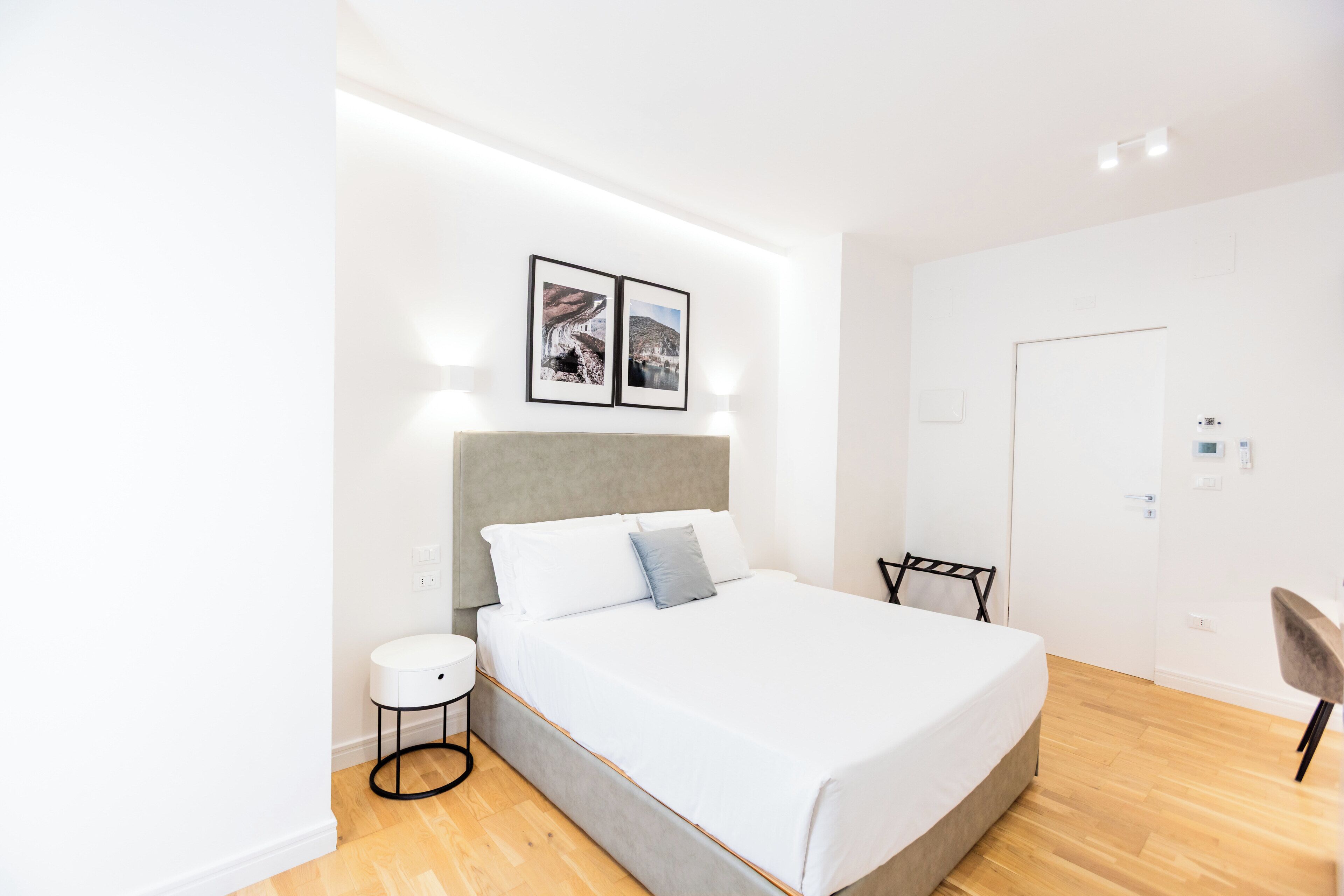 Un dormitorio moderno con una cama grande, una mesita auxiliar pequeña y dos cuadros en la pared.