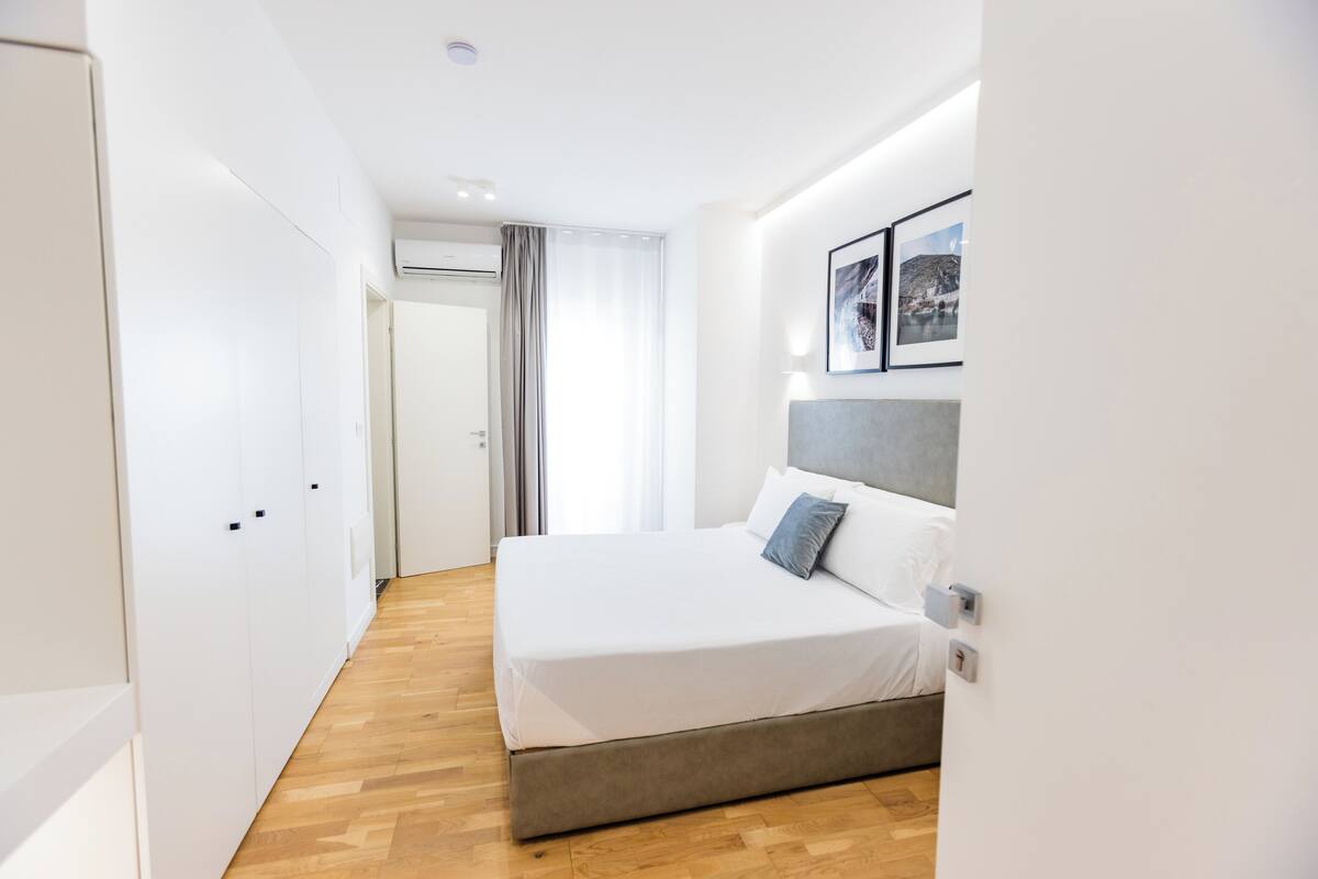 Una habitación de hotel moderna con una cama grande, un cabecero gris y suelo de madera.