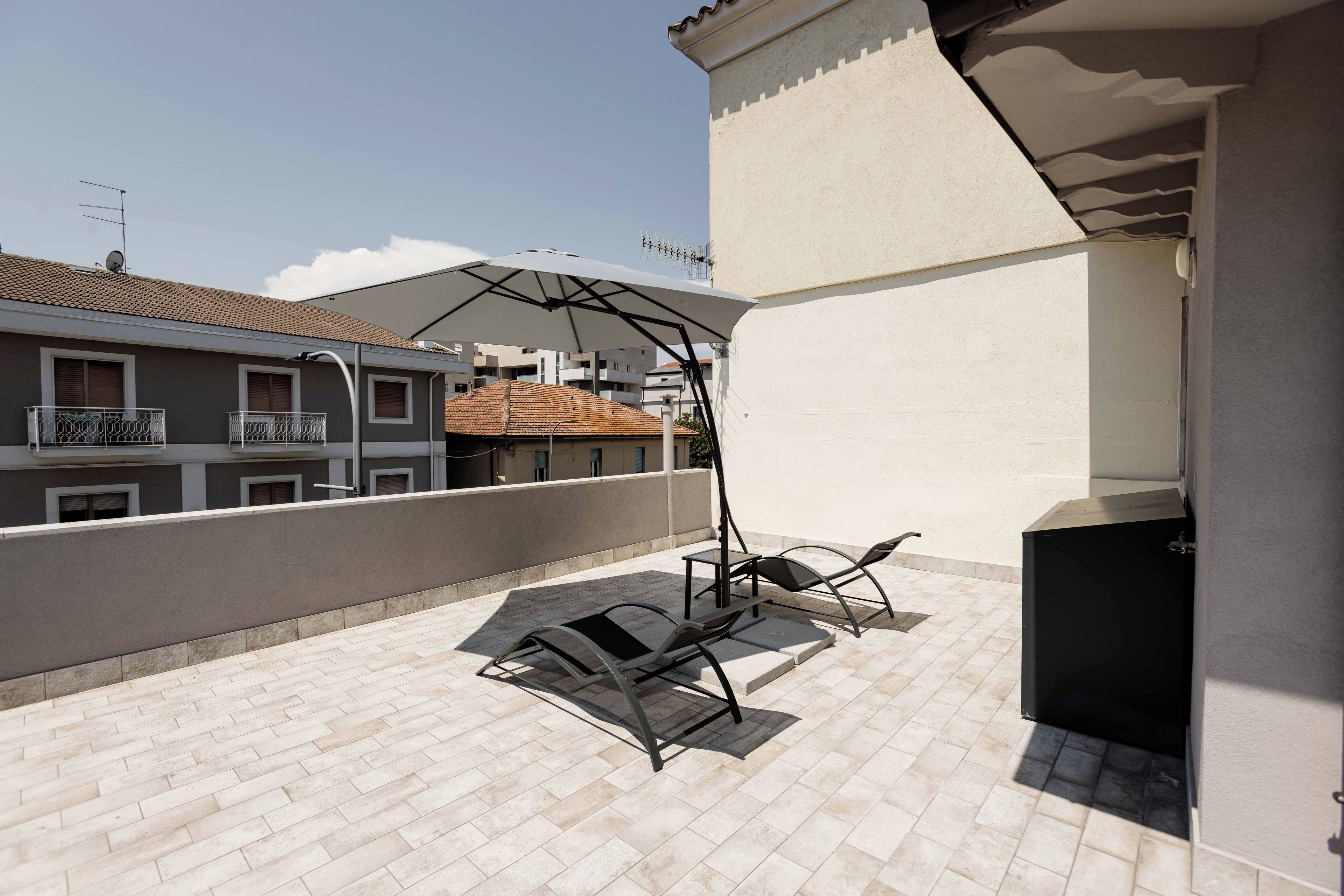 A rooftop terrace with a pergola, two lounge chairs, and a barbecue grill.