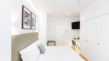 A modern hotel room with a neatly made bed, a small desk, and a TV mounted on the wall.