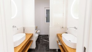 Een moderne badkamer met twee wasbakken, toilet en douche.
