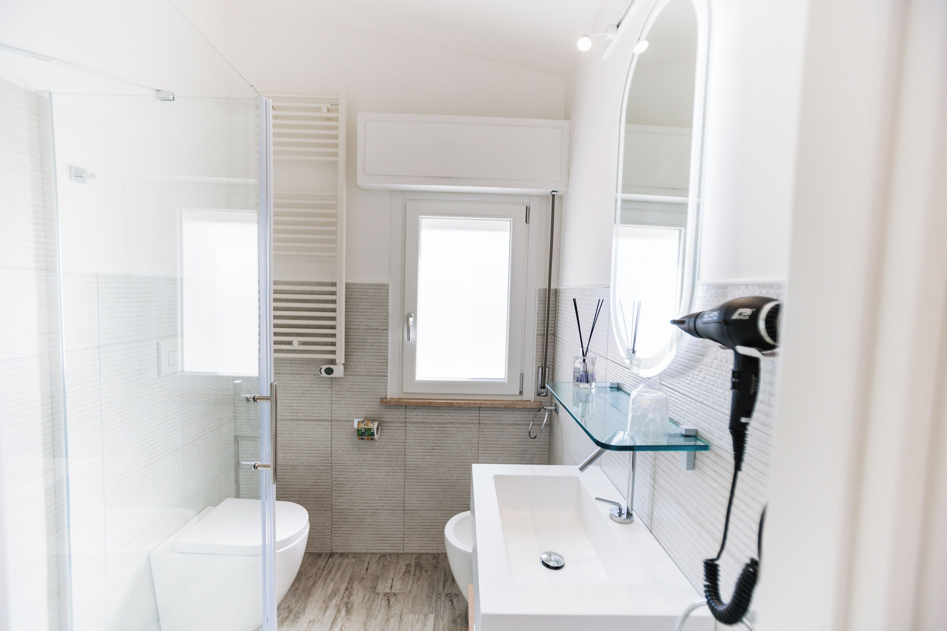 A modern bathroom with a glass shower enclosure, a white sink with a glass shelf, and a large mirror.