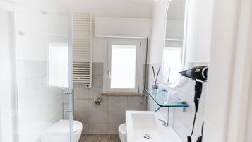 A modern bathroom with a glass shower enclosure, a white sink with a glass shelf, and a large mirror.