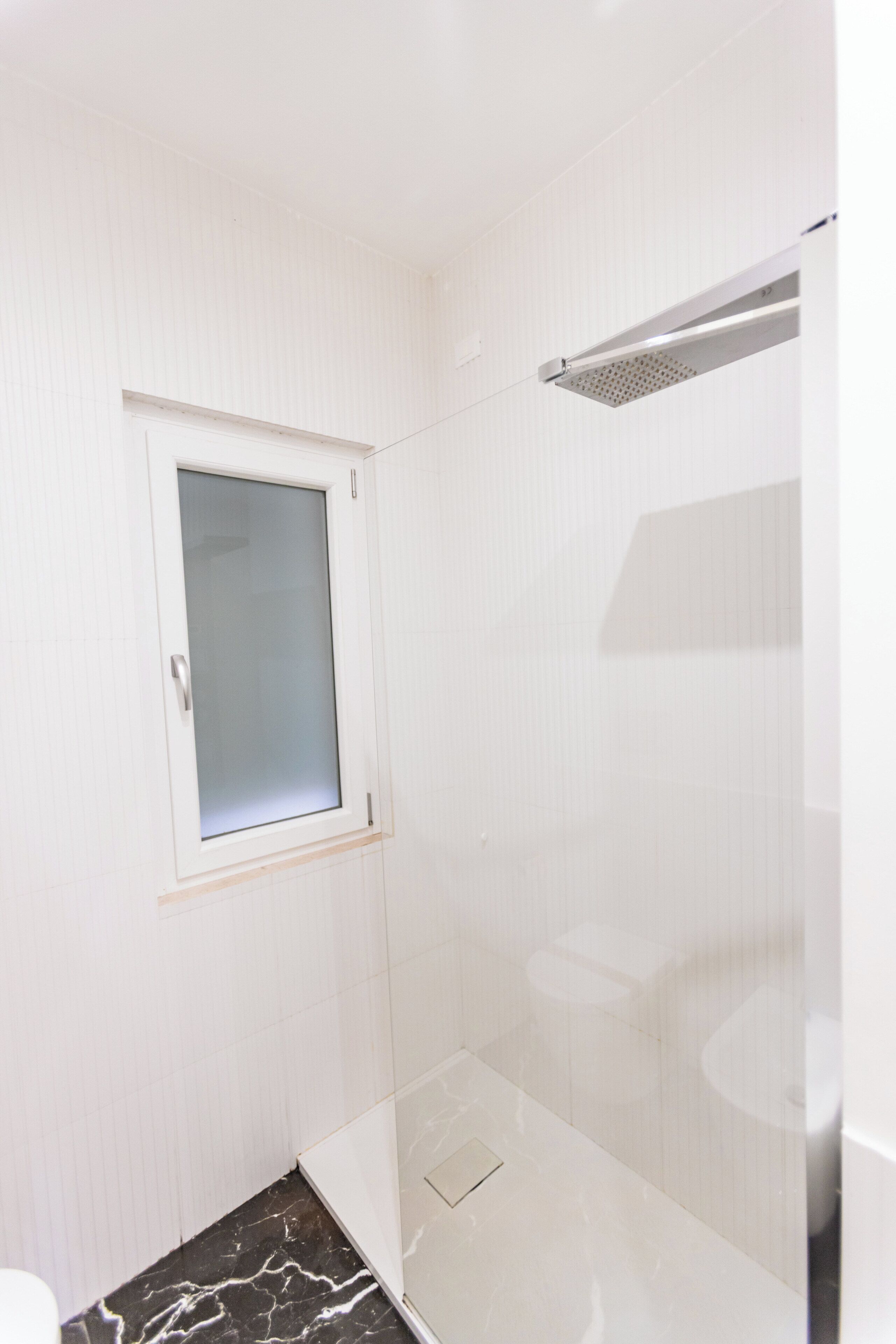 A bathroom with a shower, a toilet, and a window.