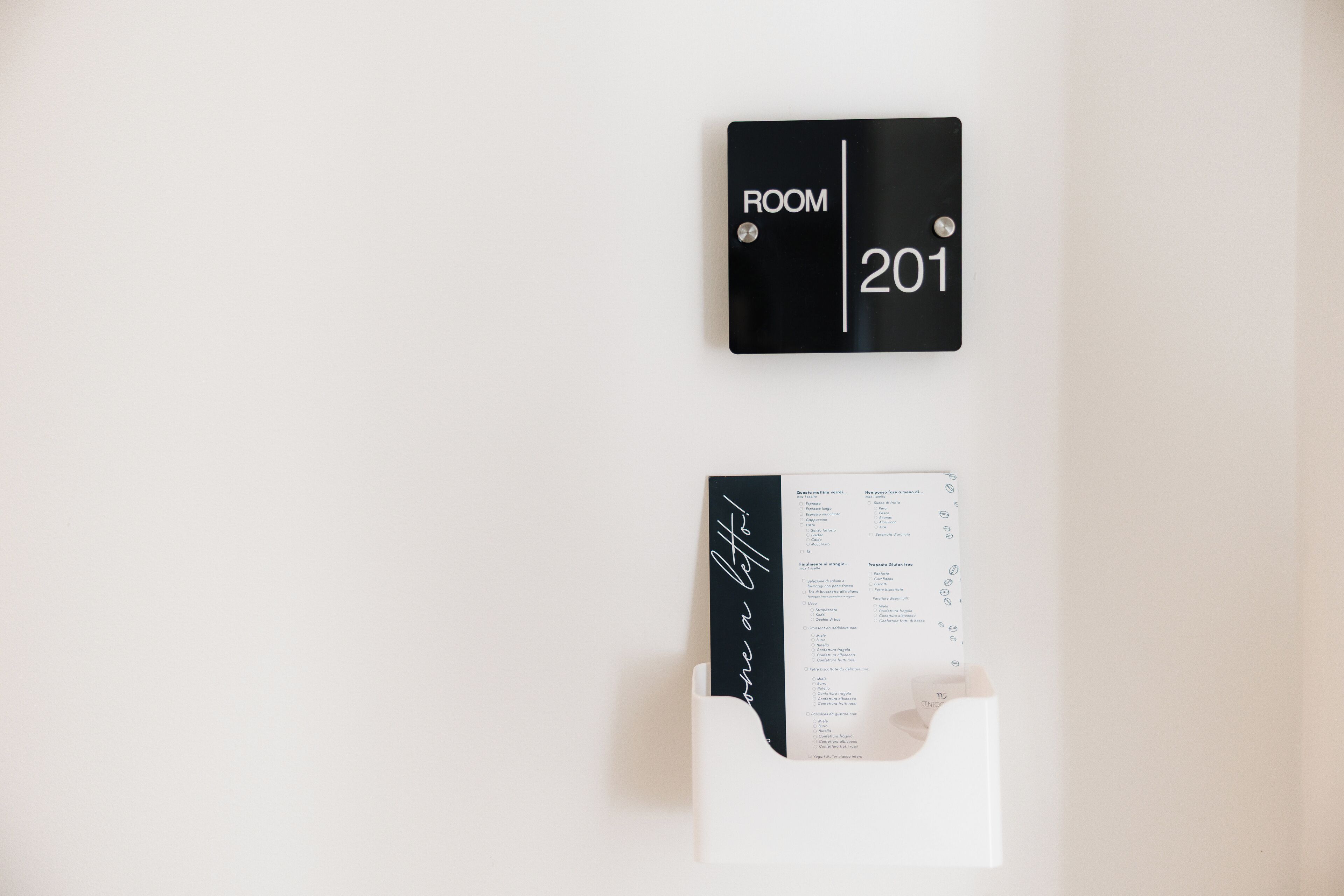 Un letrero negro con la inscripción 'ROOM 201' y una carpeta blanca con anotaciones escritas a mano.