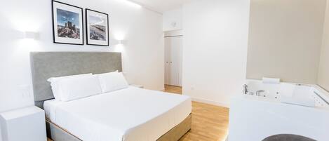 Moderni hotellihuone, jossa on suuri sänky, kylpyamme, joka on integroitu huoneeseen, ja pieni yöpöytä.