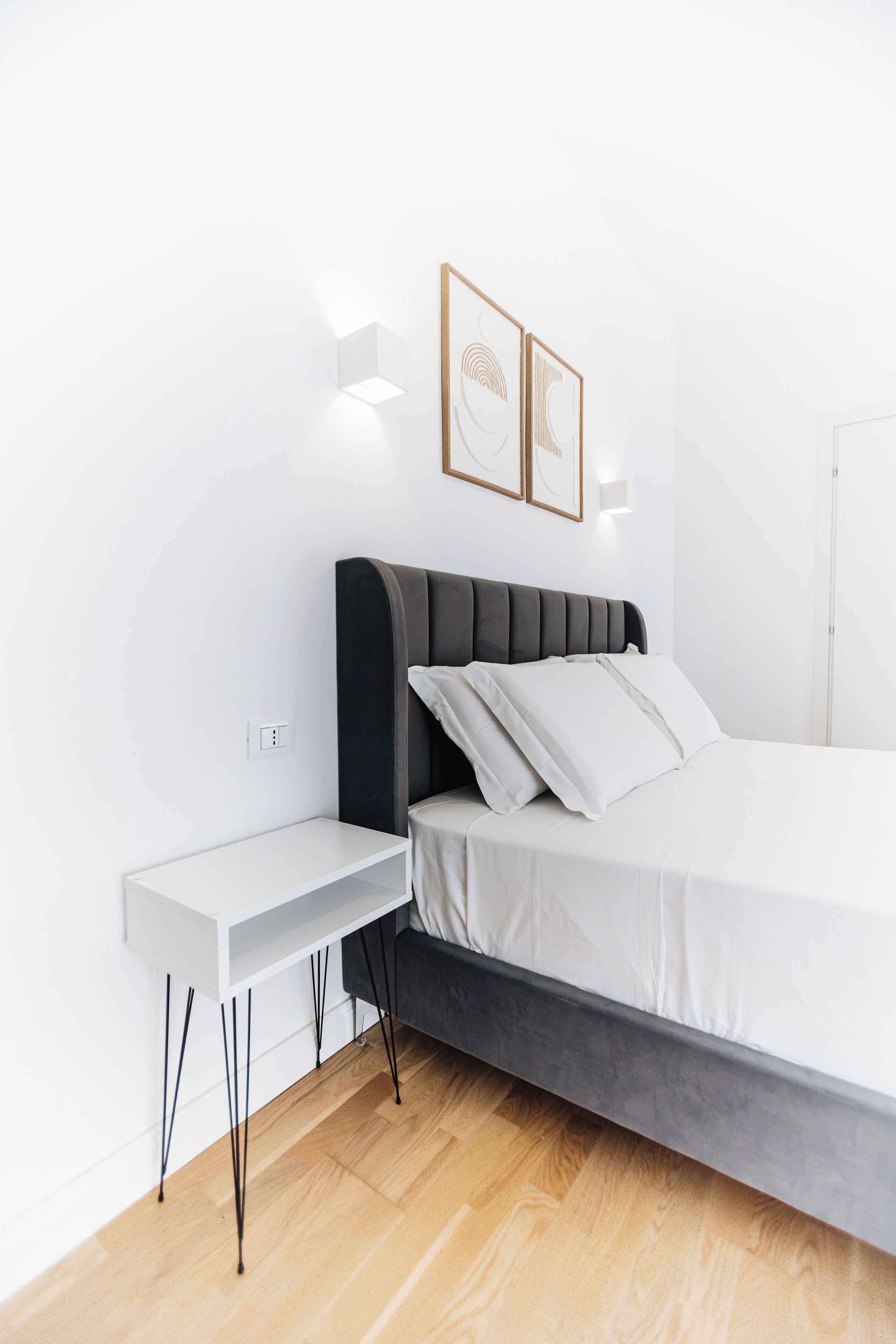 Une chambre à coucher moderne avec un lit, une table de chevet et des luminaires fixés au mur.
