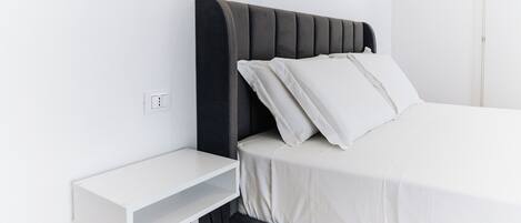 Une chambre à coucher moderne avec un lit, une table de chevet et des luminaires fixés au mur.