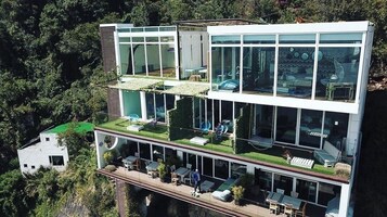 Un edificio moderno de varios pisos con amplios ventanales, terrazas al aire libre y un jardín en la azotea.