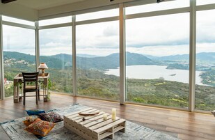 Una habitación amplia con ventanas grandes que ofrecen vistas panorámicas de un lago y colinas circundantes.