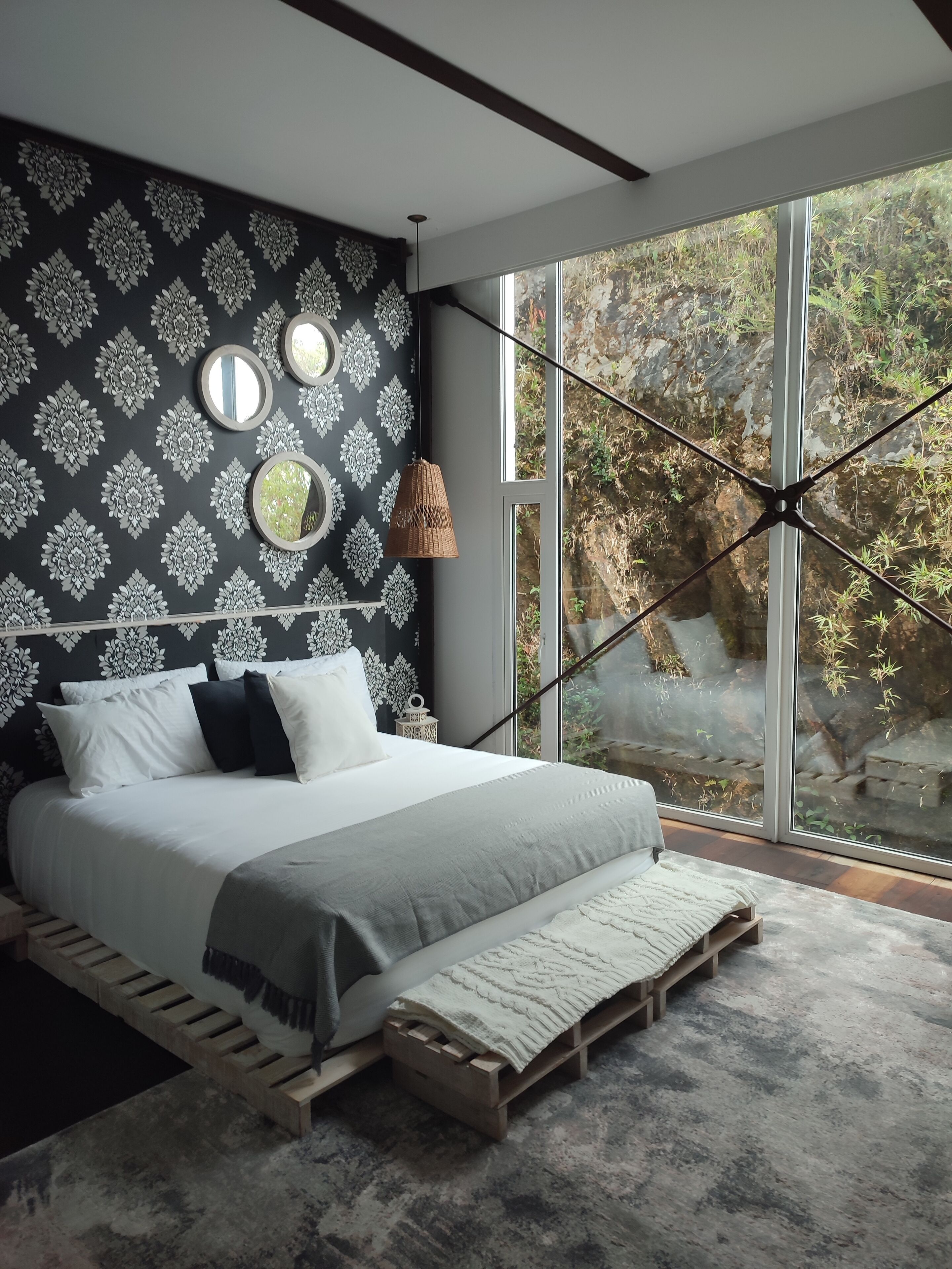 Un dormitorio moderno con una cama grande, un papel tapiz estampado y vistas a zonas verdes a través de amplios ventanales.