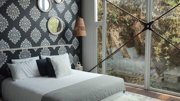 Un dormitorio moderno con una cama grande, un papel tapiz estampado y vistas a zonas verdes a través de amplios ventanales.