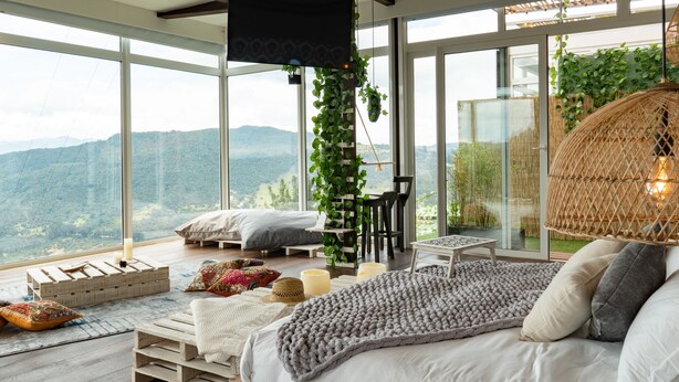 Ruime kamer met een groot bed, een kleintje tafeltje en een stoel. Er is uitzicht op bergen door grote ramen.