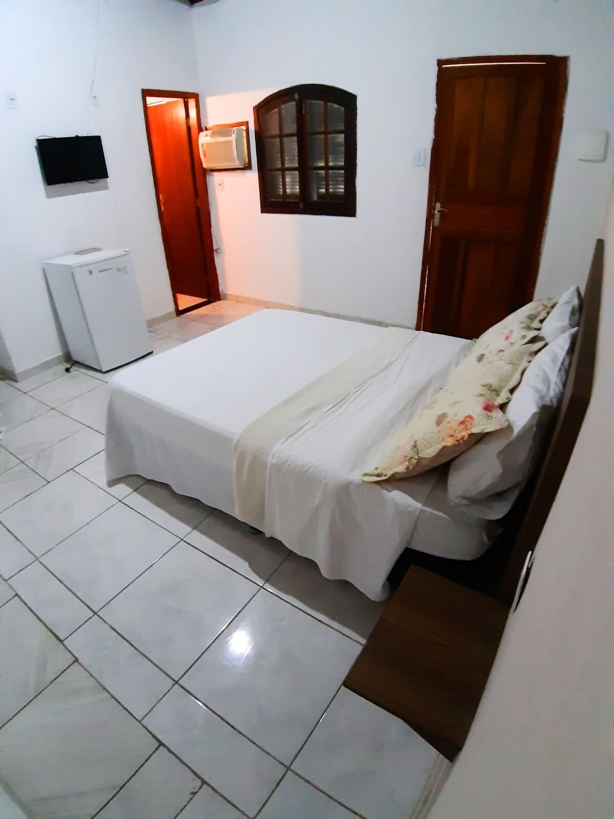 A bedroom with a bed, a small desk, a television, and a refrigerator.