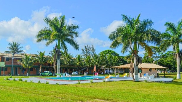 Zona de piscina con palmeras, un pequeño edificio y un automóvil.