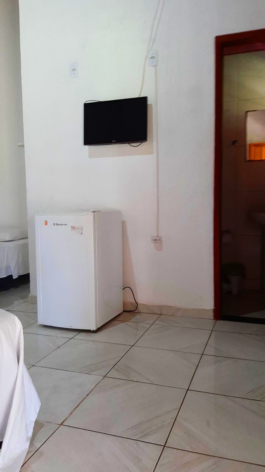 A room with a white refrigerator, a flat-screen TV mounted on the wall, and a tiled floor.