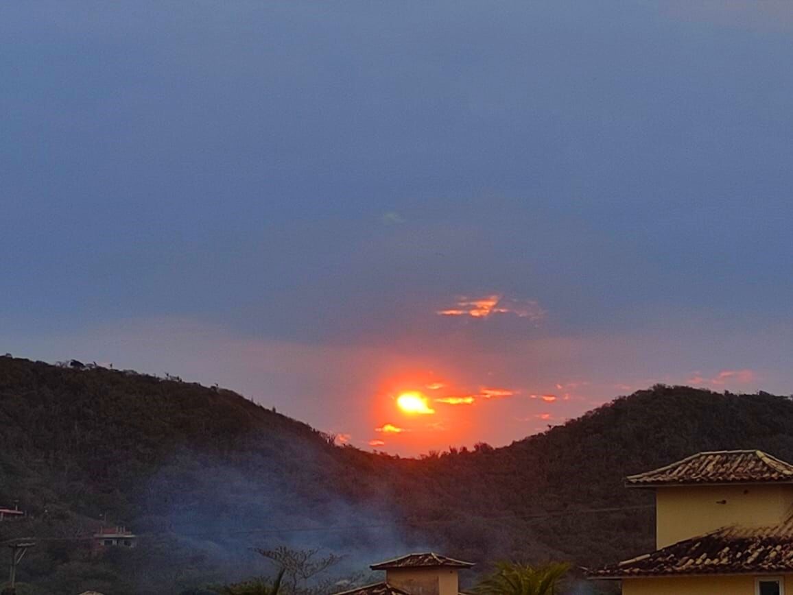 A sunset over a hilly landscape with buildings in the foreground.