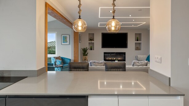 A modern kitchen with a central island, pendant lights, and a flat-screen TV above the island.