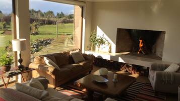 A modern living room with a fireplace, large windows, and a view of a garden.