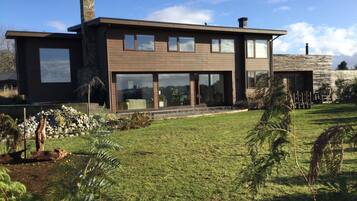 A modern two-story house with large windows, a stone chimney, and a well-maintained lawn.