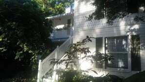 Une maison à deux étages, avec une façade blanche, un balcon visible au deuxième étage et une porte d’entrée dotée d’une fenêtre.