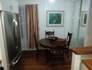 A compact kitchen with a refrigerator, wooden dining table, and chairs. - Loveday's Beach House 1 (Delray Beach)