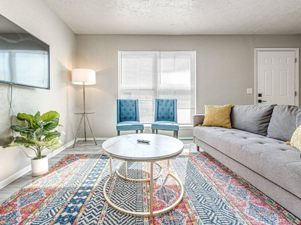 A living room with a round coffee table, two blue chairs, a grey sofa, and a colorful rug.