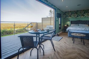Ein modernes Schlafzimmer mit einem großen Bett, einem kleinen Tisch und einem Balkon mit Blick ins Grüne.