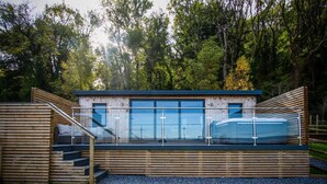 Eine moderne Holzdiele mit Glasveranda, Holzterrasse und Whirlpool.