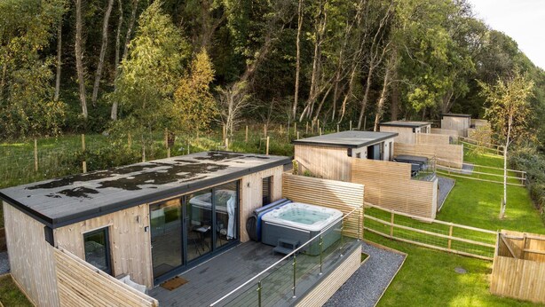 Eine moderne Holzhütte mit einem verglasten Wohnbereich, einem Whirlpool und einer Terrasse.