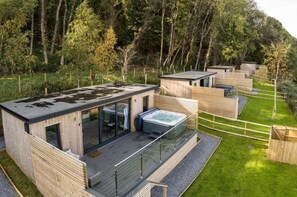 A modern outdoor cabin with a glass-enclosed living area, a hot tub, and a deck. - Brandy Cove - 1 Bed Cabin - Landimore (Swansea)