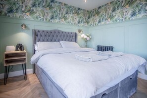 Ein Schlafzimmer mit einer gebügelten Kopfteil, einem Holznachttisch mit Lampe, einem Heizkörper und floralem Wandpapier.