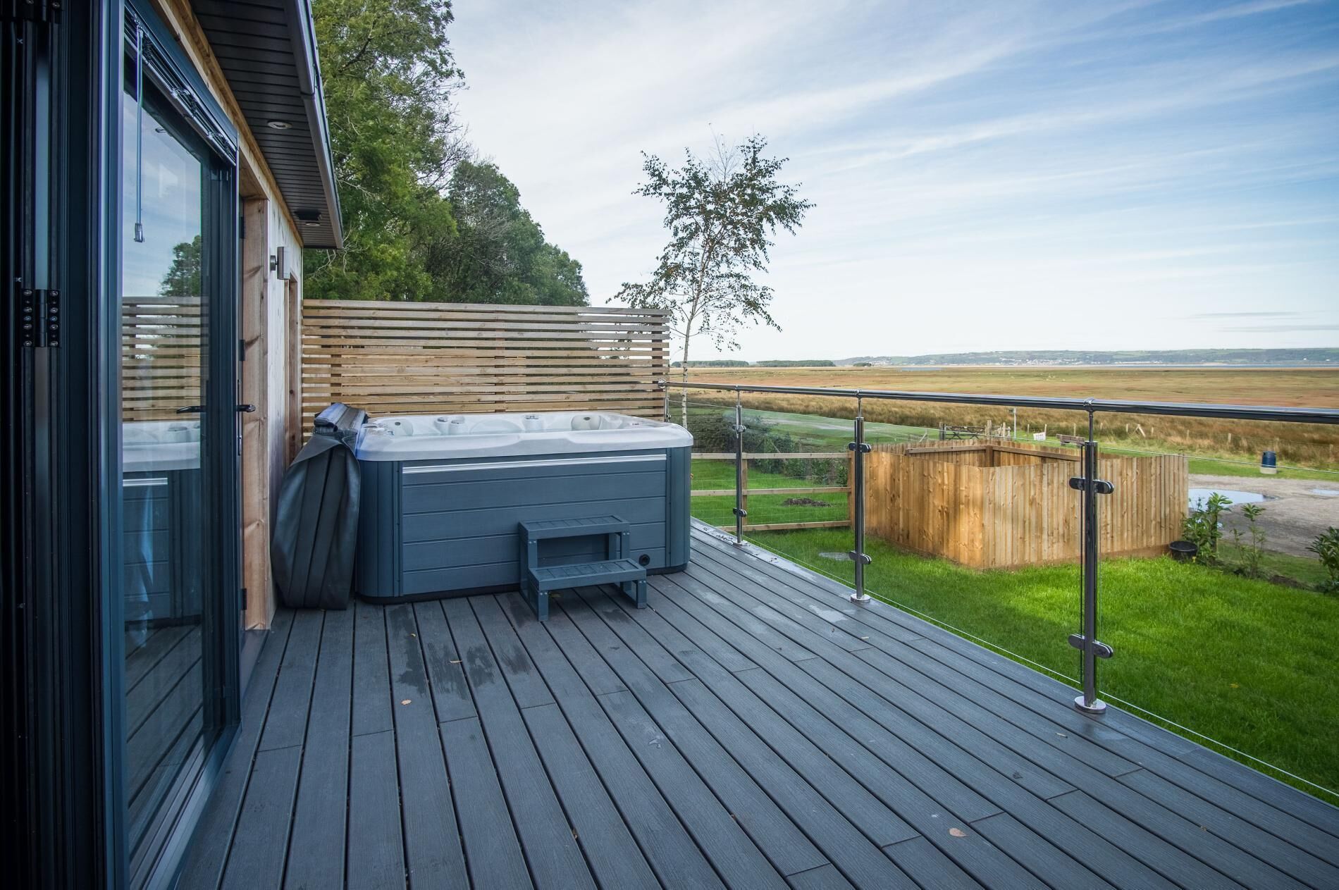 Um terraço com hidromassagem, cerca de madeira e vista para o campo.