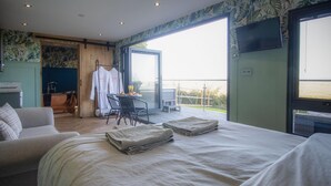 A hotel room with a bed, a sofa, a table with breakfast items, and a balcony with a view.