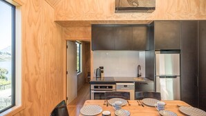 A modern kitchen with dark cabinets, stainless steel appliances, and a wooden dining table set for four. - Picture Perfect - Queenstown Holiday Home (Queenstown)