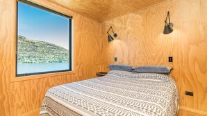 A bedroom with a large window, a bed with patterned bedding, and two wall-mounted lamps. - Picture Perfect - Queenstown Holiday Home (Queenstown)