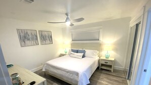 Une chambre à coucher avec un lit, des tables de chevet, un ventilateur de plafond et des œuvres d’art accrochées aux murs.