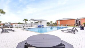 Un espace piscine comprenant des chaises longues, un petit pavillon et un coin salon abrité.