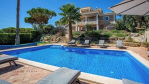 A swimming pool with lounge chairs, a stone staircase, and a two-story building in the background. - Villa Diamond (Quarteira)