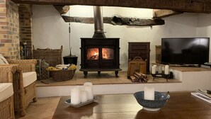 Ein gemütliches Wohnzimmer mit Kaminofen, Korbmöbeln, einem Fernseher und Kerzen auf einem Tisch.