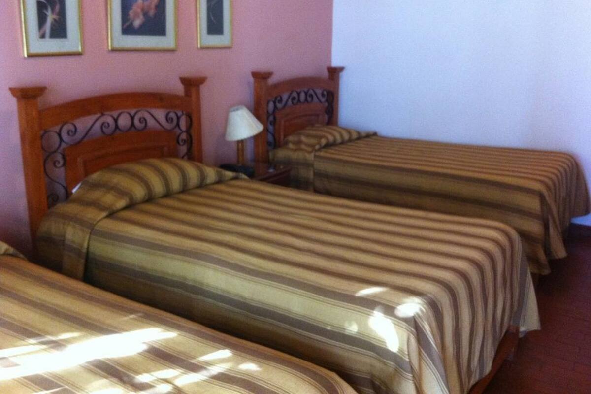 A hotel room with two single beds, a wooden headboard, a nightstand with a lamp, and framed pictures on the wall.