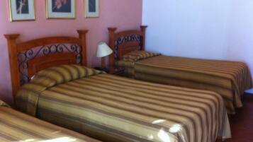 A hotel room with two single beds, a wooden headboard, a nightstand with a lamp, and framed pictures on the wall.