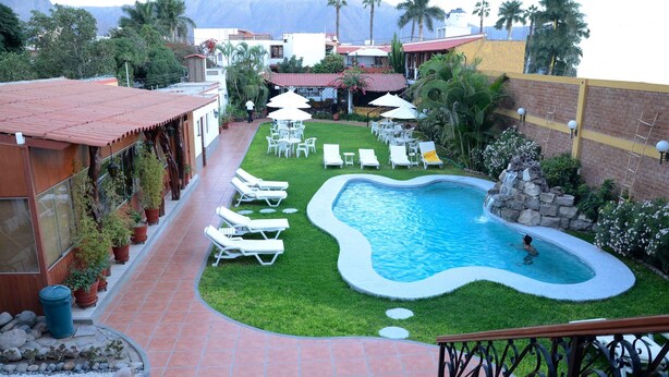 A swimming pool with a unique shape, surrounded by a well-maintained lawn and lounge chairs. - Hotel Oro Viejo (Nazca)