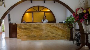 A reception desk with a marble counter, a receptionist, and a floral arrangement. - Hotel Oro Viejo (Nazca)