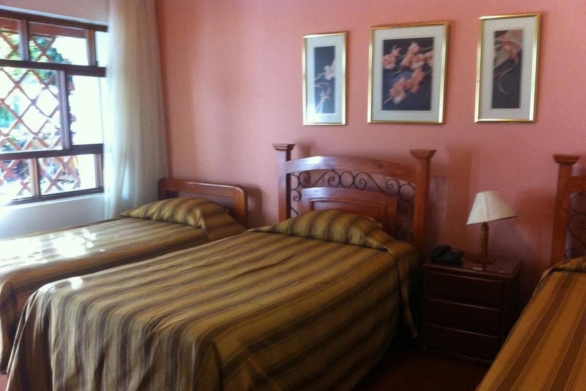 A room with two beds, a window with a lattice design, and three framed pictures on the wall.