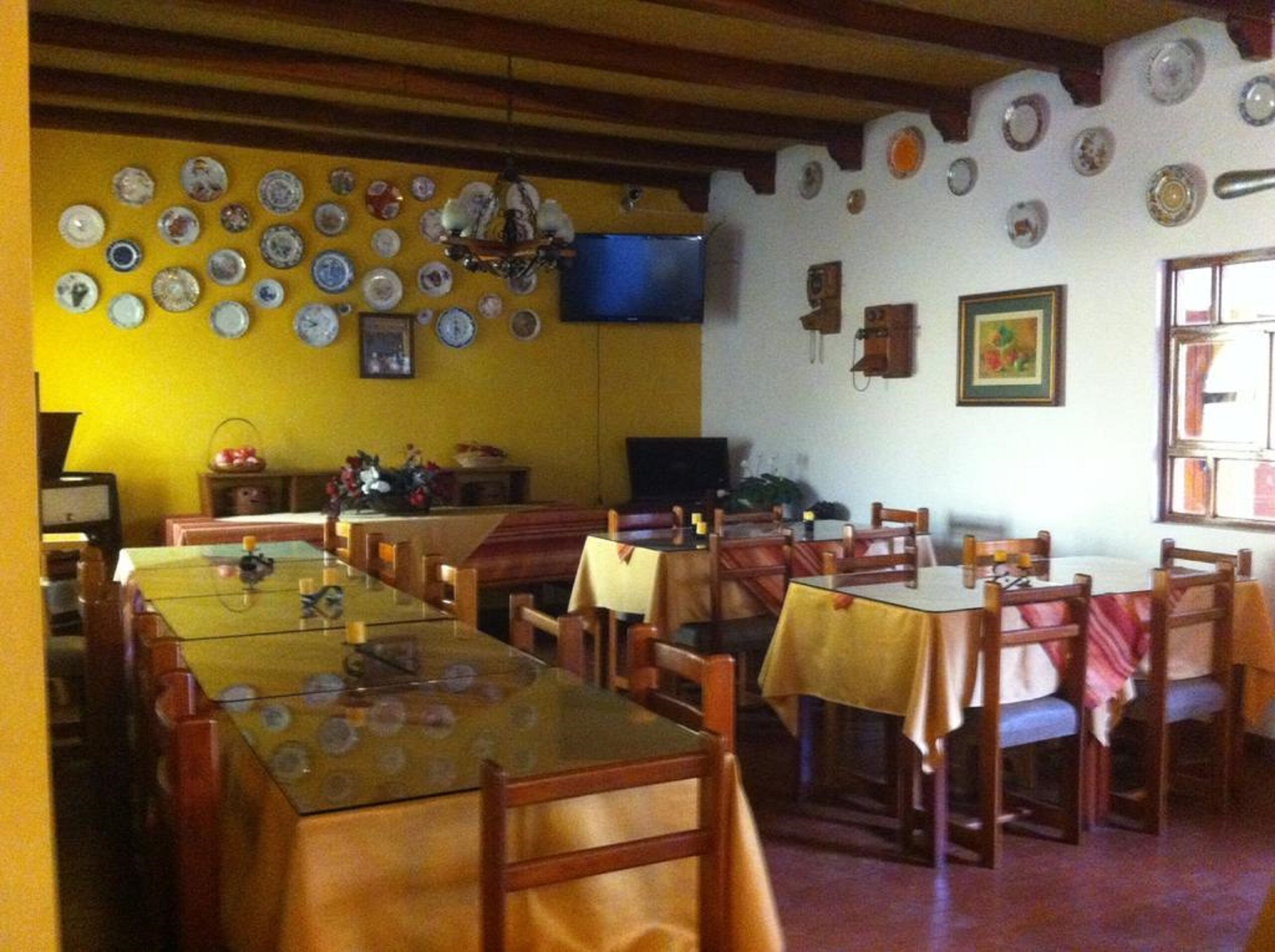 A dining area with multiple tables and chairs, a television mounted on the wall, and various decorative plates and items on the walls.