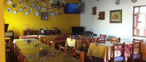 A dining area with multiple tables and chairs, a television mounted on the wall, and various decorative plates and items on the walls.
