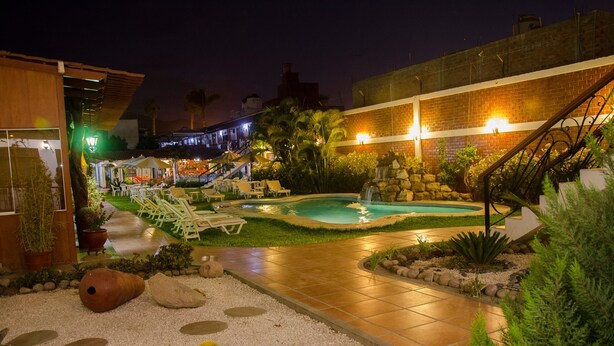 A nighttime outdoor pool area with lounge chairs, a small waterfall, and a well-lit patio. - Hotel Oro Viejo (Nazca)