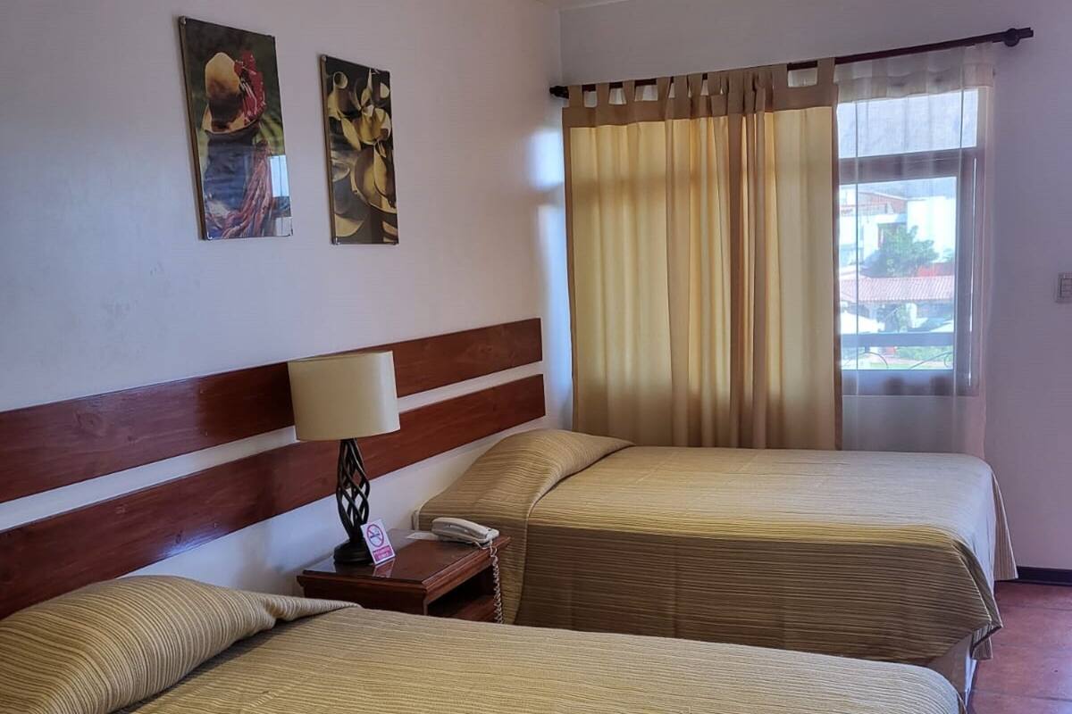A hotel room with two beds, a wooden headboard, a bedside table with a lamp, a telephone, and two framed pictures on the wall.