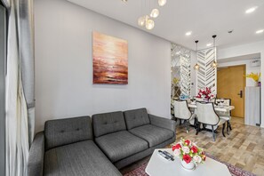 A modern living room with a grey sectional sofa, a dining table with chairs, and a large abstract painting on the wall.